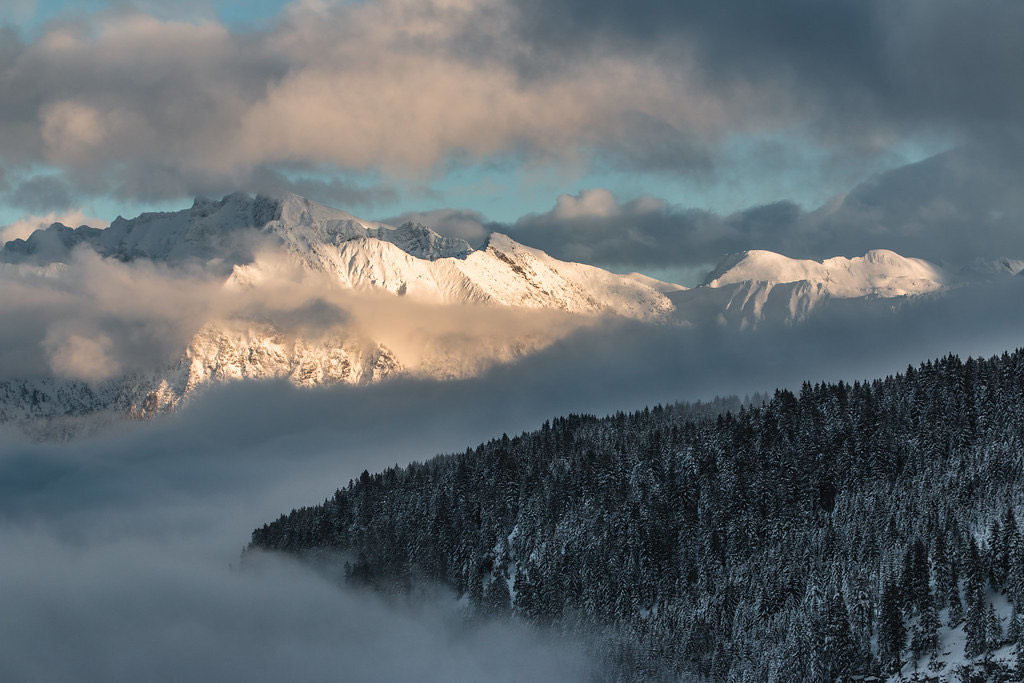 Early light breaks through cloud over a snow-dusted mountain ridge and a mist-filled valley at dawn.